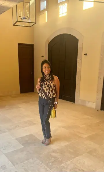 Smiling woman in a leopard print top and black pants, holding a yellow bag.