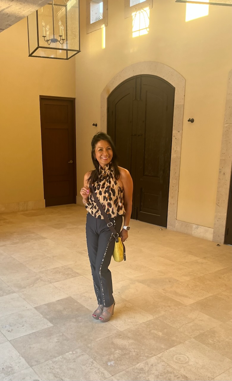 Smiling woman in a leopard print top and black pants, holding a yellow bag.